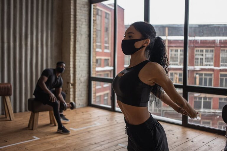 Two athletes exercising indoors with masks for safety during pandemic.