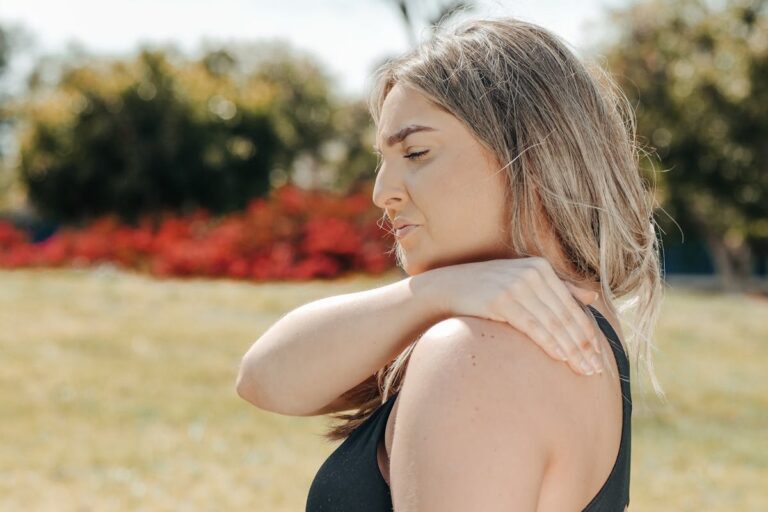 Woman in black tank top touching shoulder outdoors. Concept of shoulder pain and relaxation.
