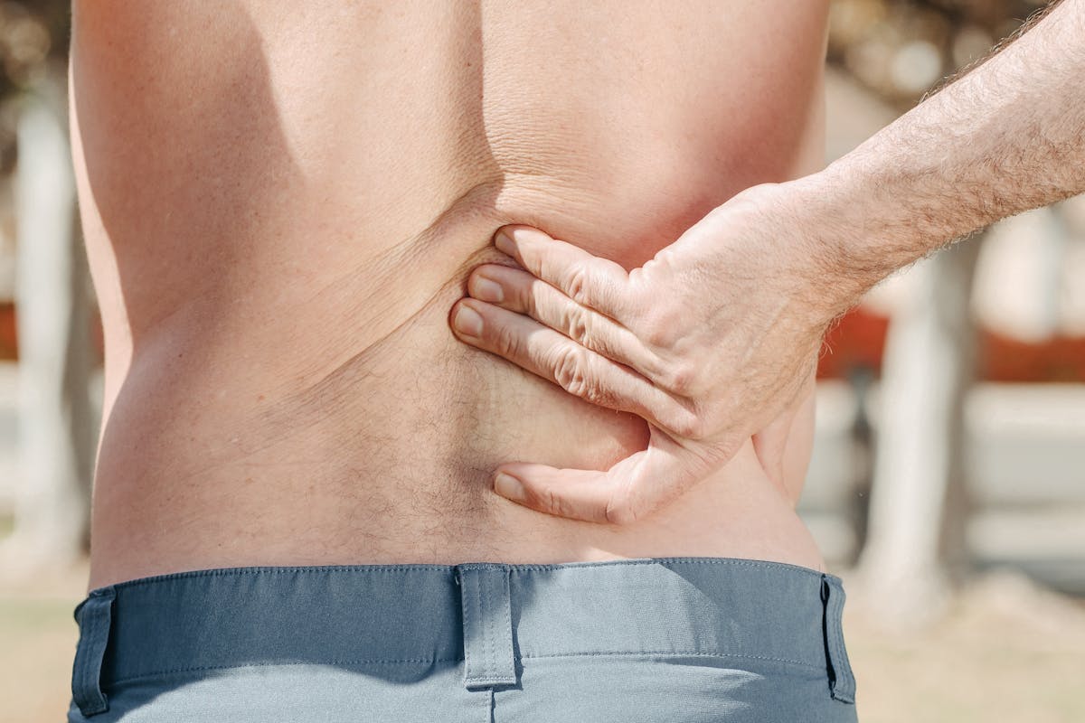 Close-up of a man holding his lower back in pain, possibly indicating discomfort or injury.