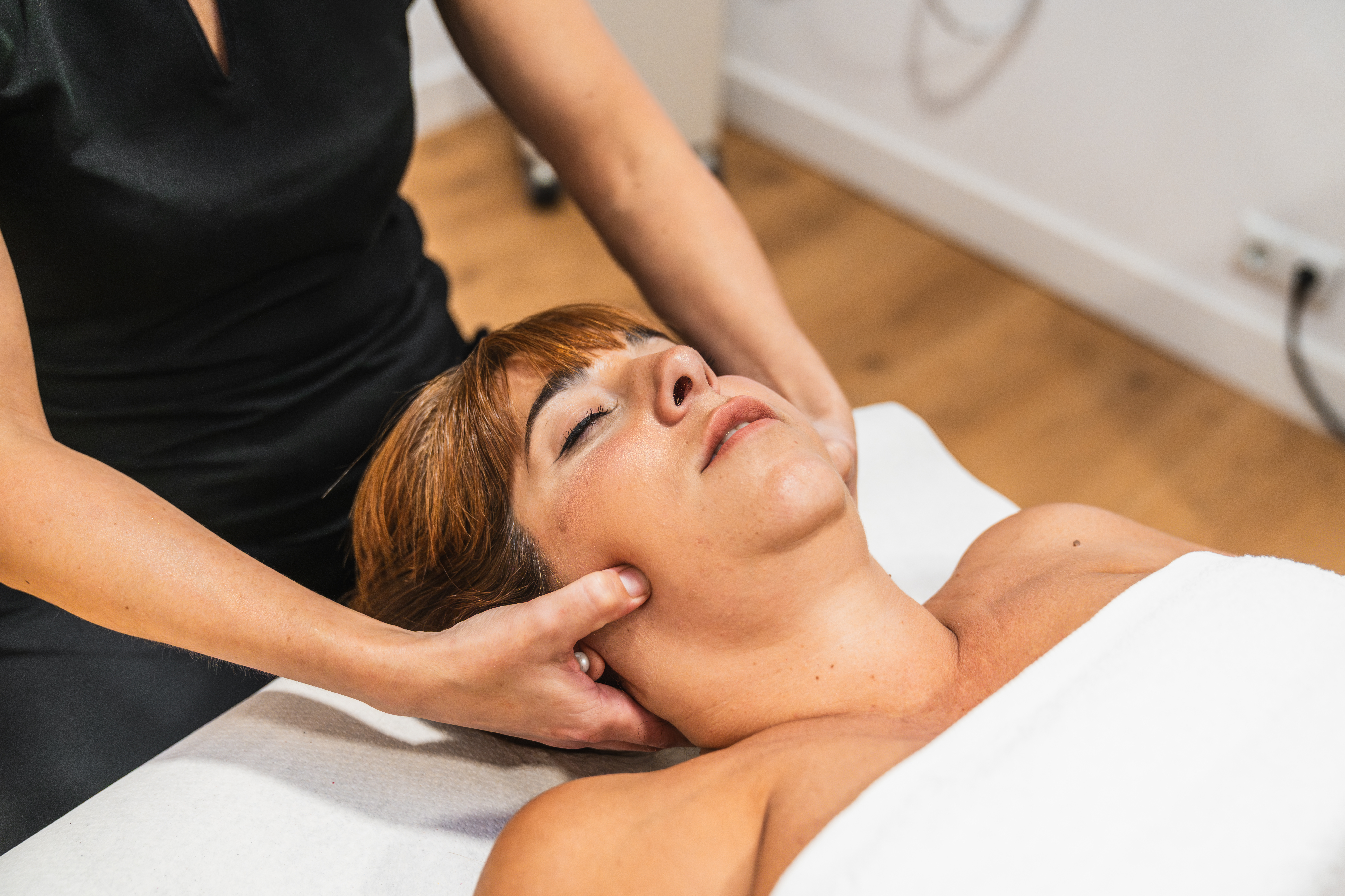 Professional therapist performing physiotherapeutic massage on a woman's jaw and neck to alleviate tmj disorder symptoms